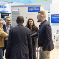 Visitors share insights and smiles while networking at the JST Power Equipment booth, Smarter E Europe 2025, Messezentrum München. Group of professionals networking and smiling at the JST Power Equipment booth during Smarter E Europe 2025 in Munich.