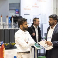 Engaged discussion between JST Power representatives at The Smarter E Europe 2025, highlighting advanced power technologies and customer solutions. Two professionals in conversation at a trade show booth, discussing technical materials in front of power equipment displays