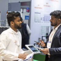 Engaged discussion between JST Power representatives at The Smarter E Europe 2025, highlighting advanced power technologies and customer solutions. Two professionals in conversation at a trade show booth, discussing technical materials in front of power equipment displays.