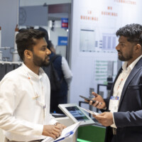 Engaged discussion between JST Power representatives at The Smarter E Europe 2025, highlighting advanced power technologies and customer solutions. Two professionals in conversation at a trade show booth, discussing technical materials in front of power equipment displays.