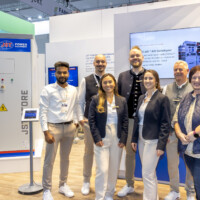 The JST Power team showcasing their Battery Energy Storage System (BESS) at The Smarter E Europe 2025, highlighting innovation in sustainable energy solutions. JST Power team poses in front of their exhibition booth at The Smarter E Europe 2025, with a Battery Energy Storage System displayed behind them.