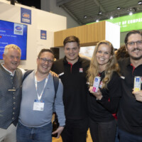JST team and partners enjoying the vibrant atmosphere at Smarter E Europe 2025, celebrating new collaborations and innovations. Group of five smiling people at an exhibition booth during Smarter E Europe 2025, posing together with drinks in hand and wearing event badges.