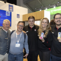 JST team and partners enjoying the vibrant atmosphere at Smarter E Europe 2025, celebrating new collaborations and innovations. Group of five smiling people at an exhibition booth during Smarter E Europe 2025, posing together with drinks in hand and wearing event badges.