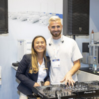 Friendly faces at The Smarter E Europe 2025 — showcasing innovative energy solutions alongside a DJ setup, blending technology and vibrant event atmosphere. Two JST Power team members at The Smarter E Europe 2025 event booth with DJ equipment and electrical components in the background.