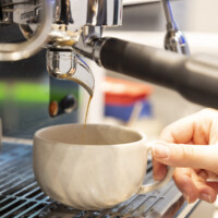 A fresh espresso being prepared from a machine onto a white mug Close-up of a coffee machine pouring espresso into a ceramic mug held by a hand at an exhibition booth