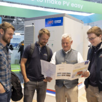 Visitors at the JST Power’s booth at The Smarter E Europe 2025 Four men reading a JST Power Equipment brochure in front of a battery energy storage unit at The Smarter E Europe 2025.