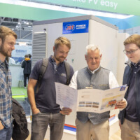 Visitors at the JST Power’s booth at The Smarter E Europe 2025 Four men reading a JST Power Equipment brochure in front of a battery energy storage unit at The Smarter E Europe 2025.