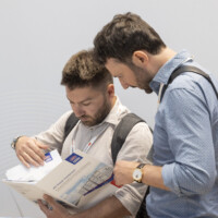 Attendees study technical brochures at the JST Power Equipment booth during Smarter E Europe 2025 at Messezentrum München. Two male visitors closely examining a JST Power Equipment product brochure at Smarter E Europe 2025 in Munich.