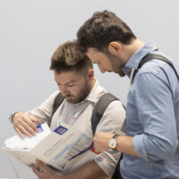 Attendees study technical brochures at the JST Power Equipment booth during Smarter E Europe 2025 at Messezentrum München. Two male visitors closely examining a JST Power Equipment product brochure at Smarter E Europe 2025 in Munich.